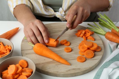 Woman cutting fresh carrot at white table, closeup