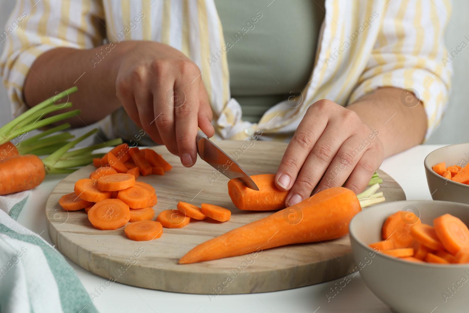 Photo of Woman cutting fresh carrot at table, closeup