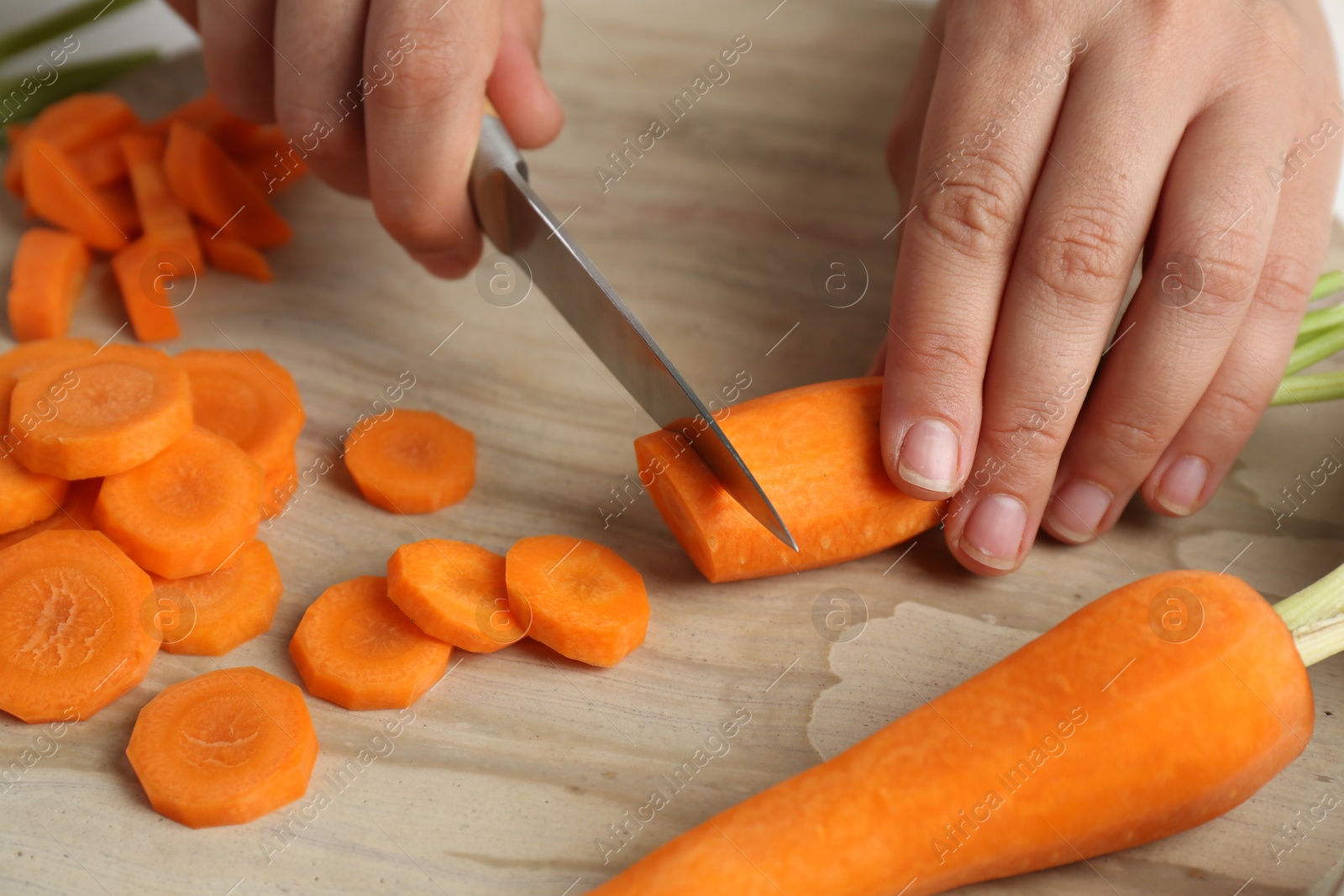 Photo of Woman cutting fresh carrot at table, closeup