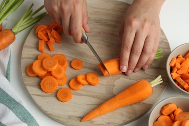 Woman cutting fresh carrot at table, closeup