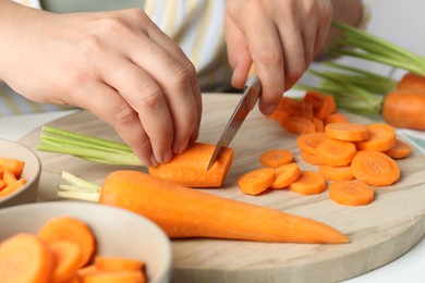 Photo of Woman cutting fresh carrot at table, closeup