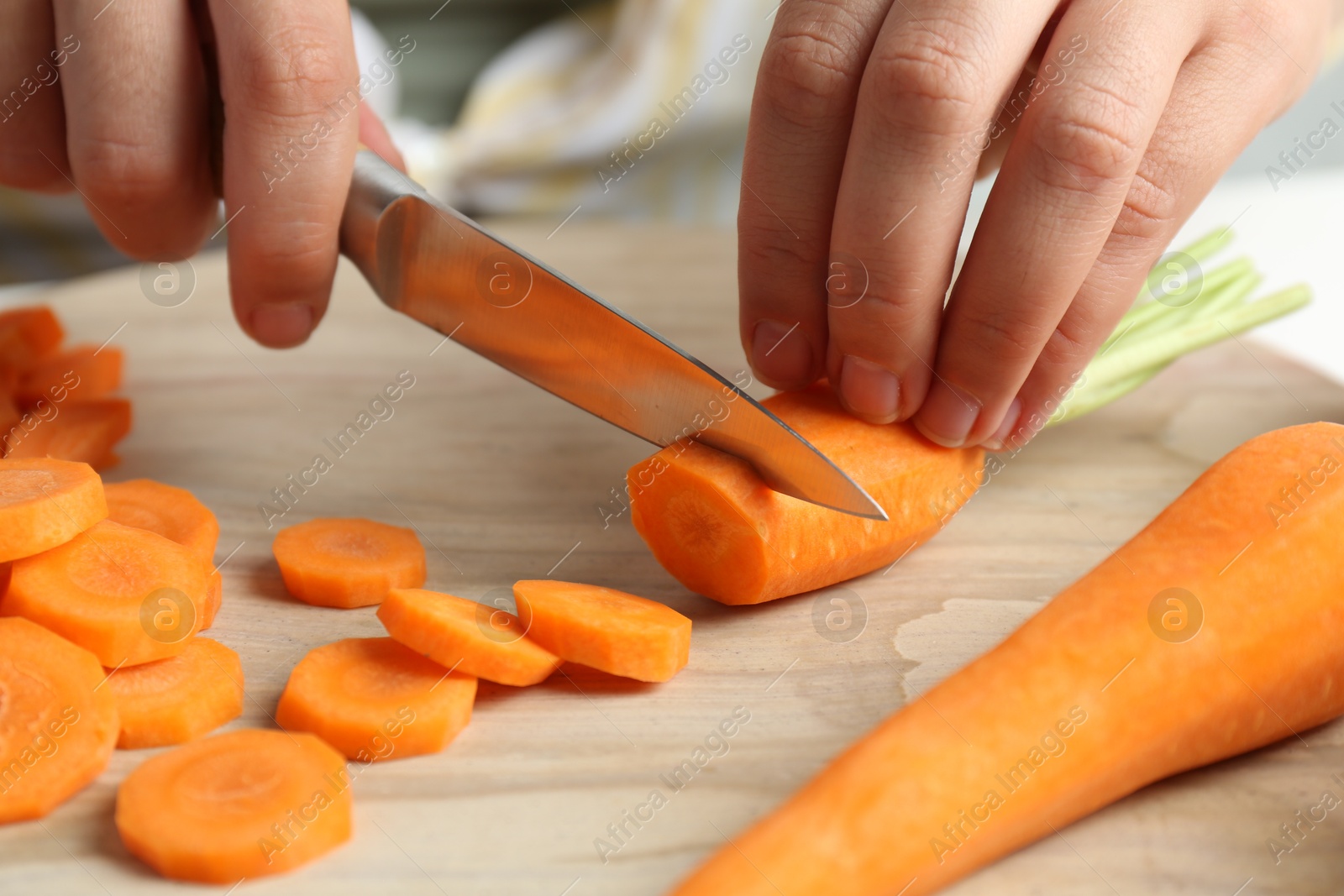 Photo of Woman cutting fresh carrot at table, closeup