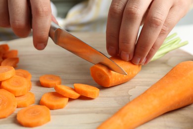 Photo of Woman cutting fresh carrot at table, closeup