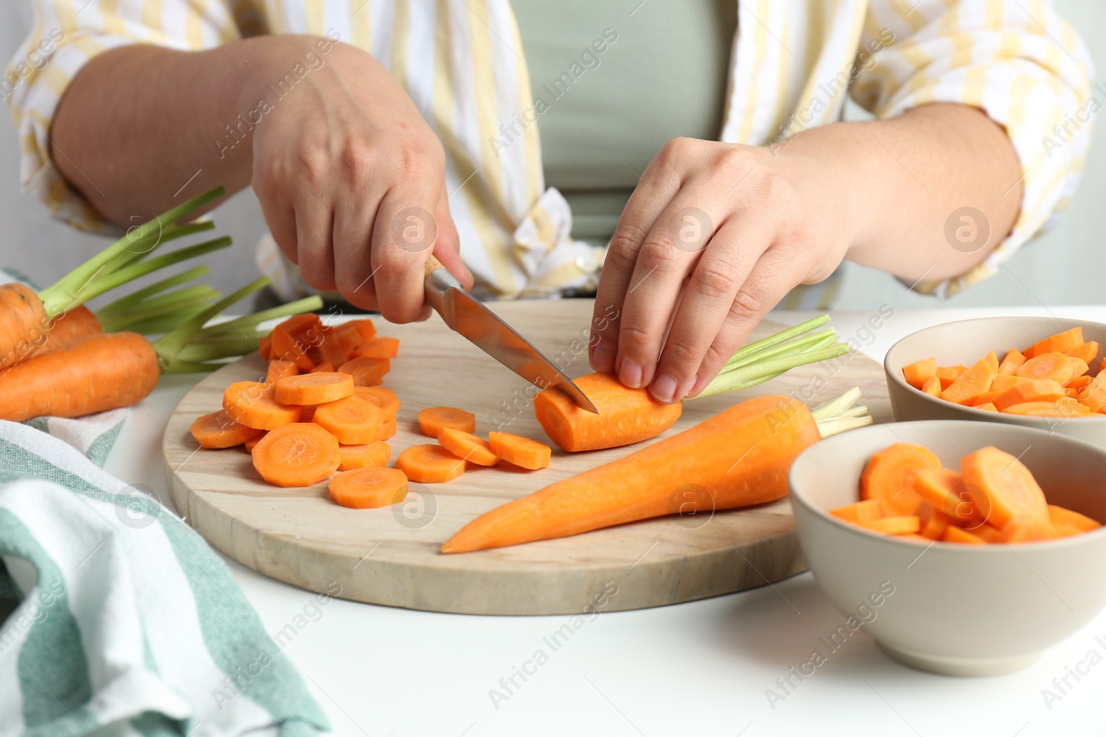 Photo of Woman cutting fresh carrot at white table, closeup