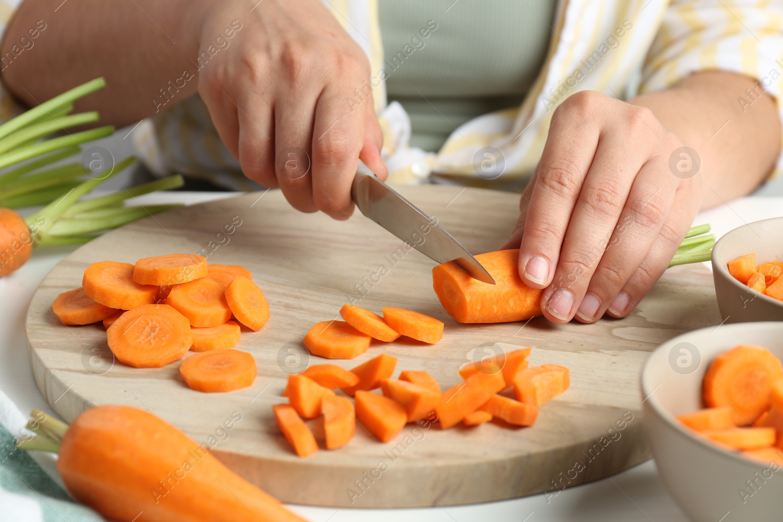 Photo of Woman cutting fresh carrot at table, closeup