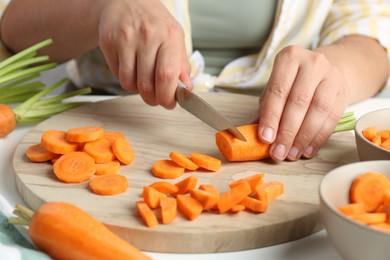 Photo of Woman cutting fresh carrot at table, closeup