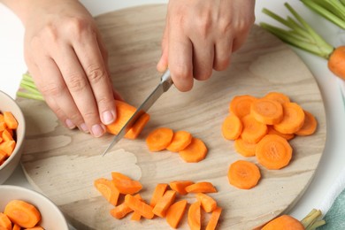 Photo of Woman cutting fresh carrot at table, closeup