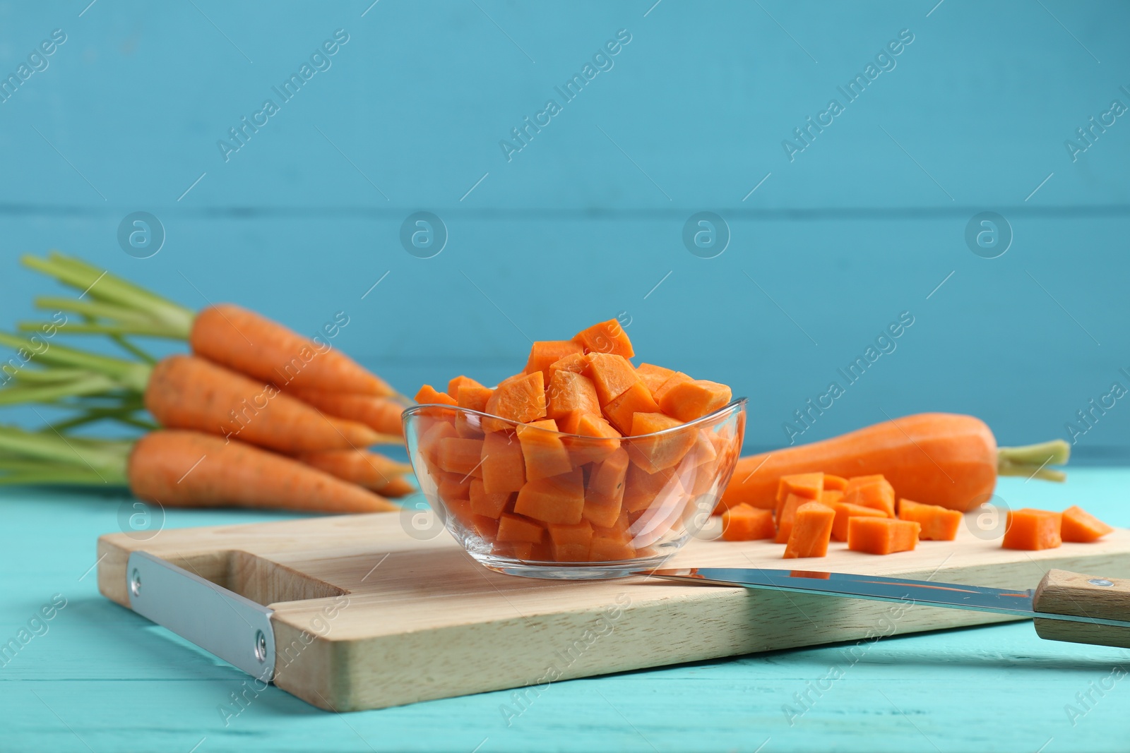 Photo of Delicious chopped carrot in bowl and knife on light blue wooden table, closeup