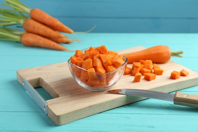 Photo of Delicious chopped carrot in bowl and knife on light blue wooden table, closeup