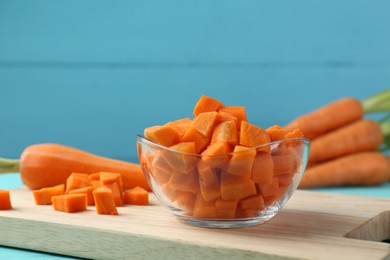 Delicious chopped carrot in bowl on table against light blue wooden background, closeup