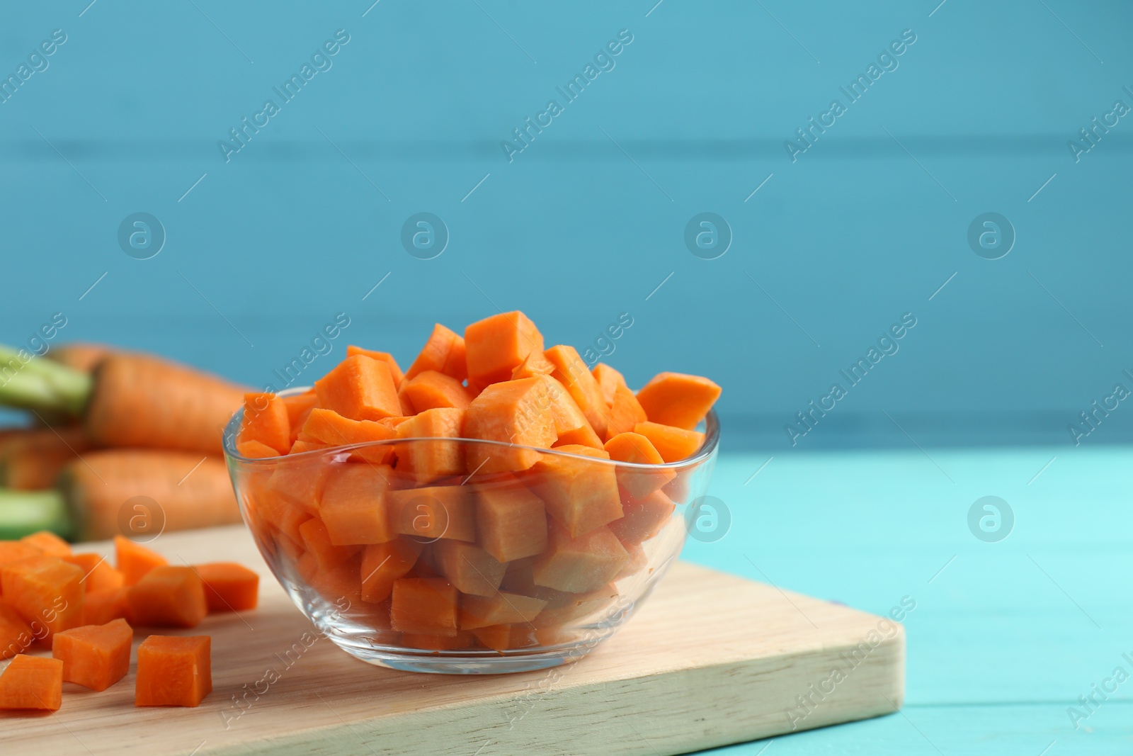 Photo of Delicious chopped carrot in bowl on light blue wooden table, space for text