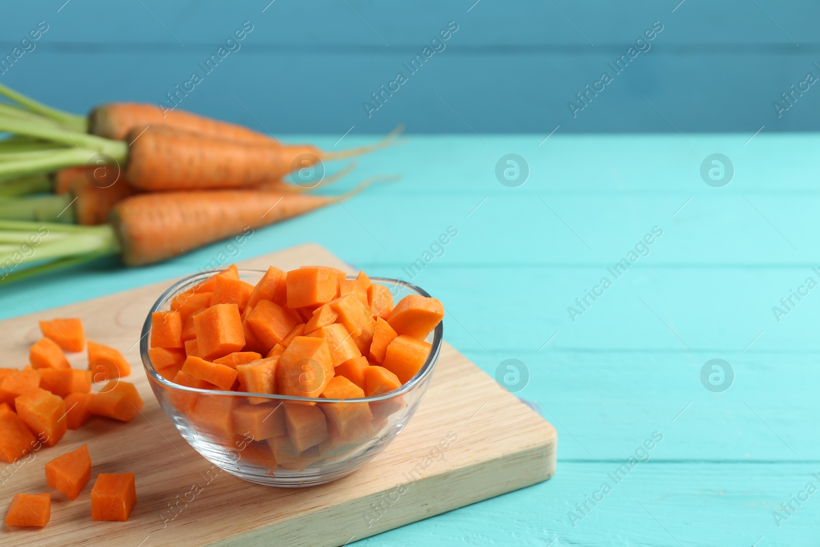 Photo of Delicious chopped carrot in bowl on light blue wooden table, space for text