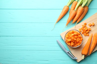 Chopped carrot in bowl, fresh vegetables and peeler on light blue wooden table, flat lay. Space for text