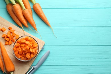 Photo of Chopped carrot in bowl, fresh vegetables and peeler on light blue wooden table, flat lay. Space for text