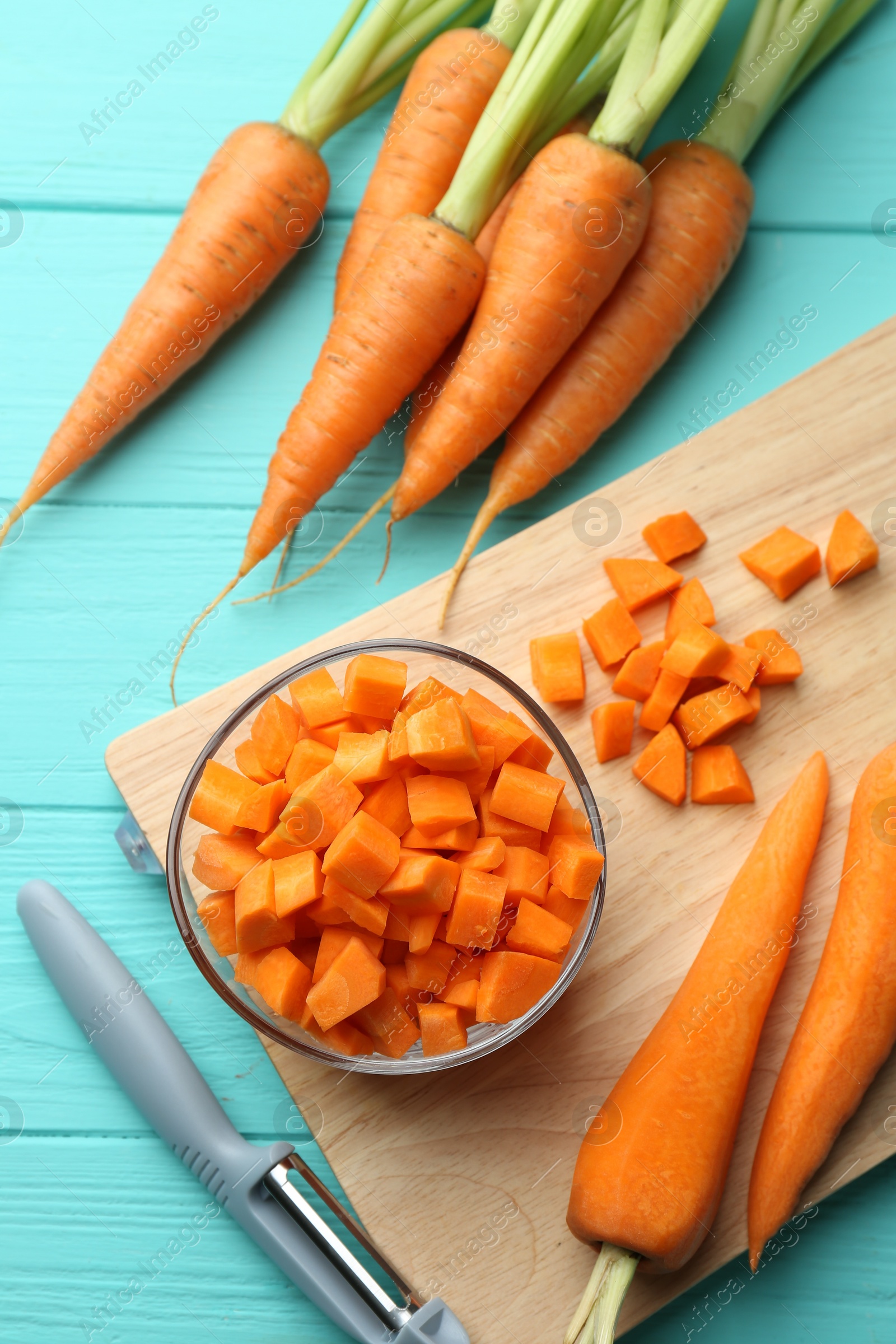 Photo of Chopped carrot in bowl, fresh vegetables and peeler on light blue wooden table, flat lay