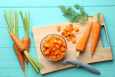 Photo of Chopped carrot in bowl, fresh vegetables and peeler on light blue wooden table, flat lay