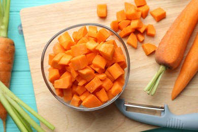 Photo of Chopped carrot in bowl, fresh vegetables and peeler on light blue wooden table, top view