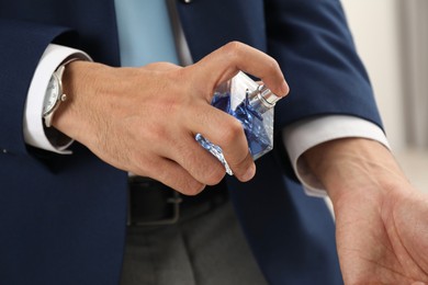 Young man spraying luxury perfume indoors, closeup