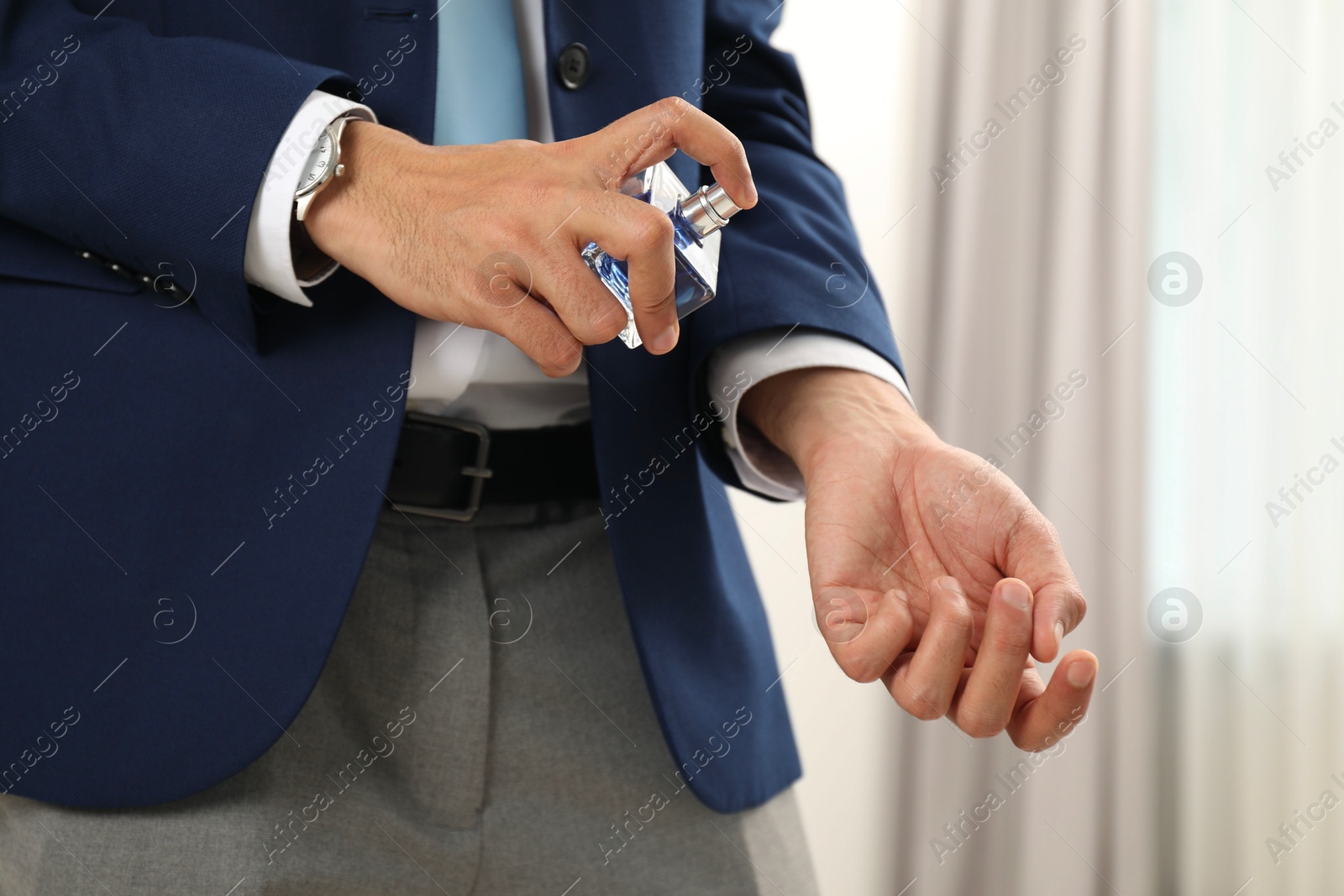 Photo of Young man spraying luxury perfume indoors, closeup