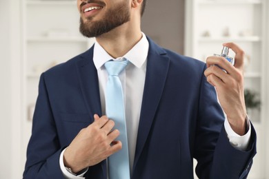 Young man spraying luxury perfume indoors, closeup