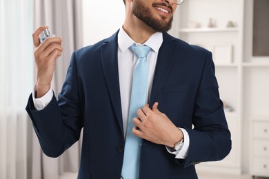 Photo of Young man spraying luxury perfume indoors, closeup