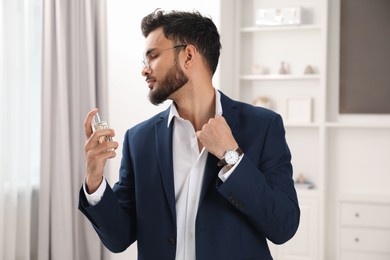 Attractive young man spraying luxury perfume indoors