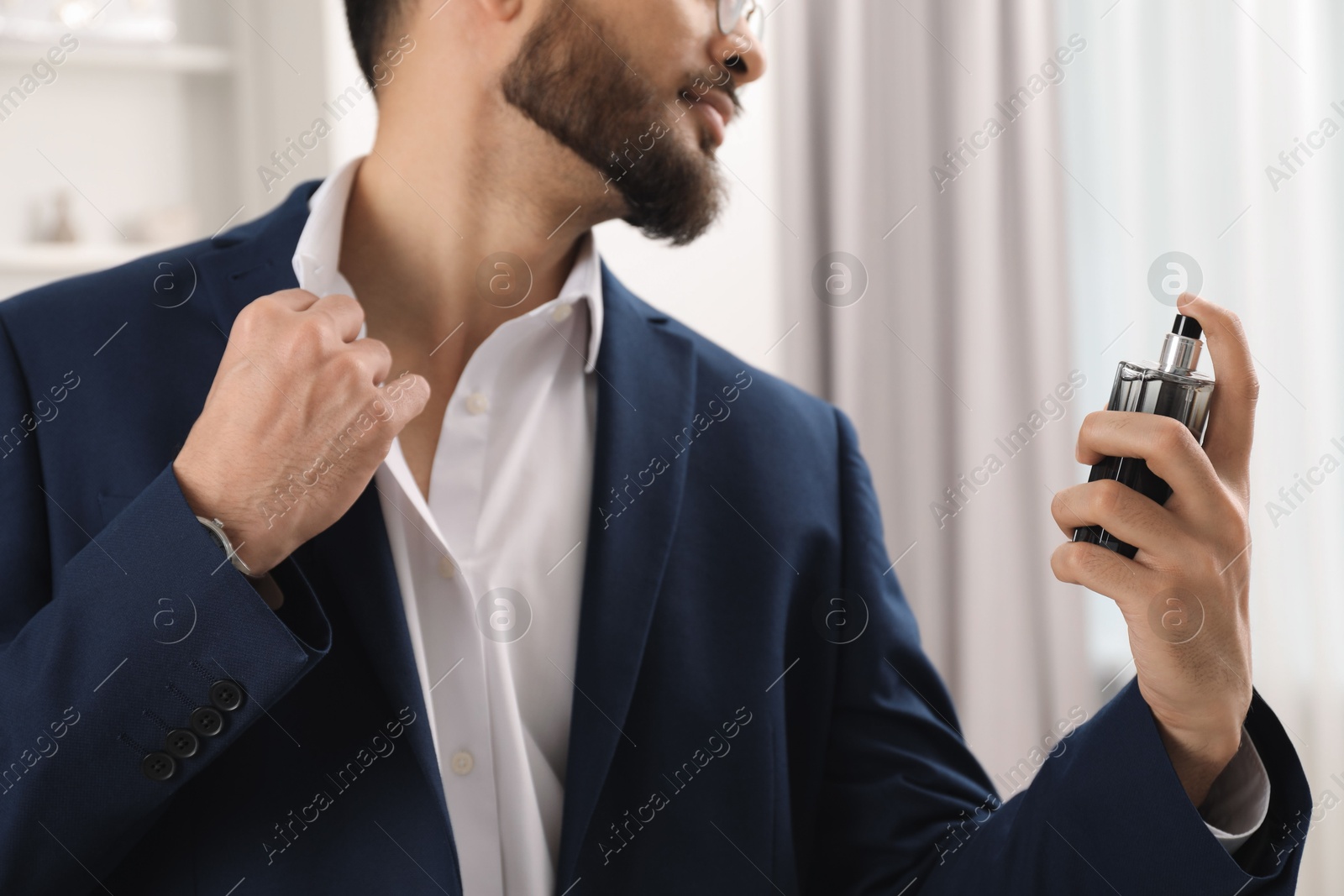 Photo of Young man spraying luxury perfume indoors, closeup