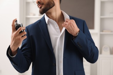 Photo of Young man spraying luxury perfume indoors, closeup