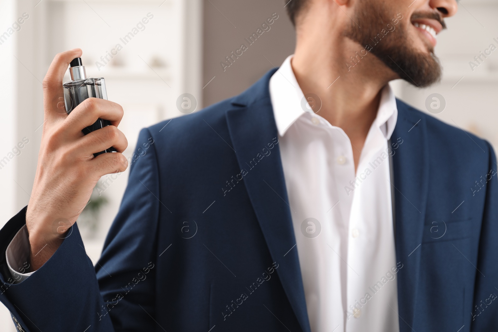 Photo of Young man spraying luxury perfume indoors, closeup