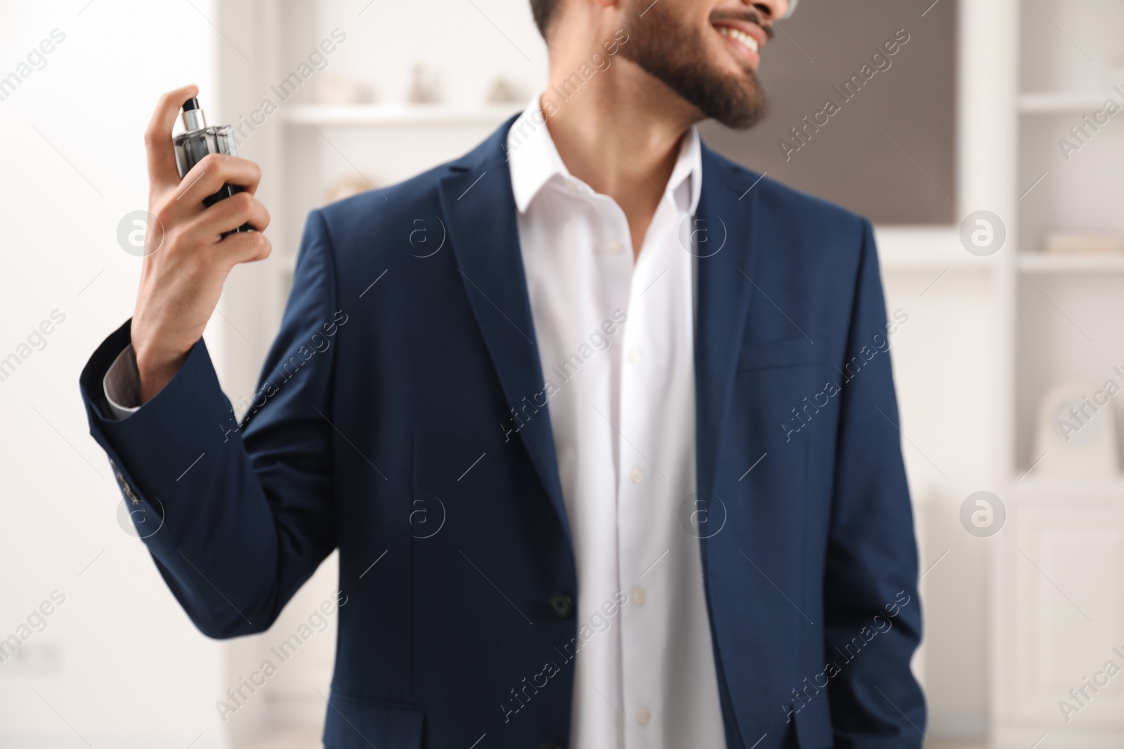 Photo of Young man spraying luxury perfume indoors, closeup