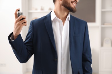 Young man spraying luxury perfume indoors, closeup