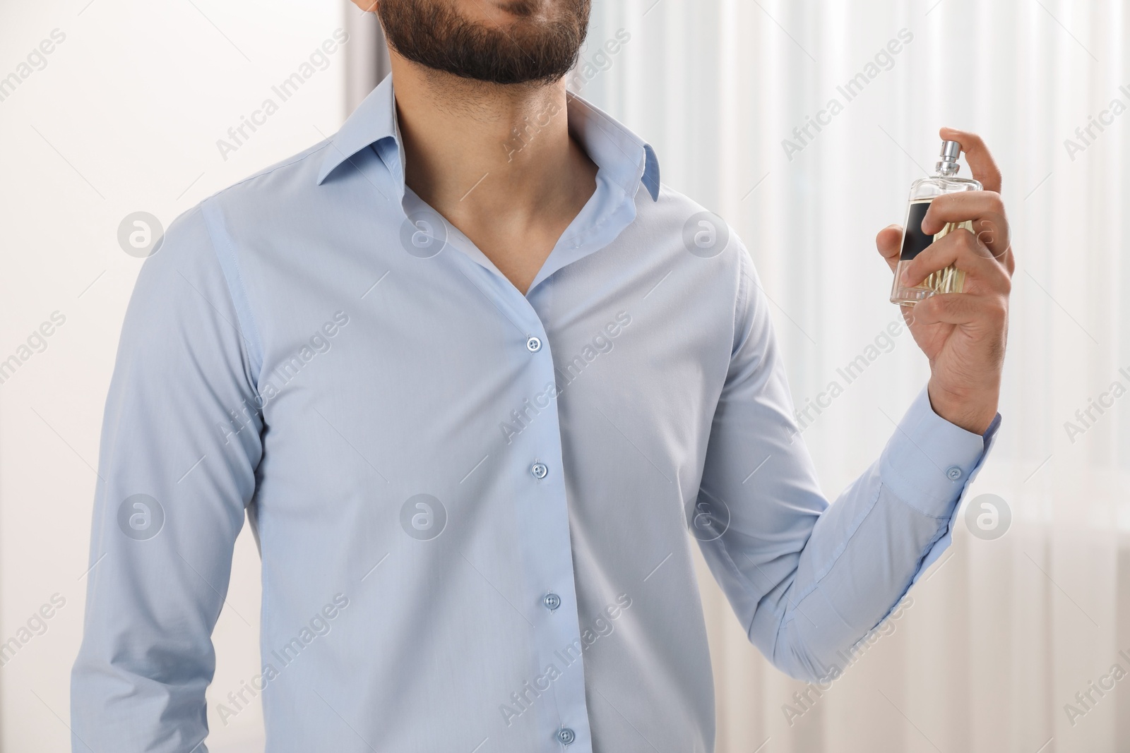 Photo of Young man spraying luxury perfume indoors, closeup