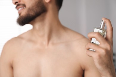 Young man spraying luxury perfume indoors, closeup