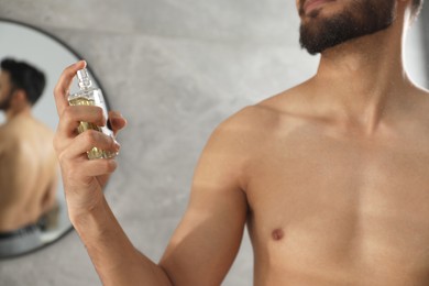 Young man spraying luxury perfume indoors, closeup