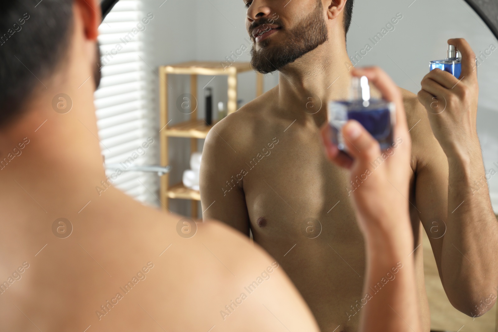 Photo of Man spraying luxury perfume near mirror indoors, closeup