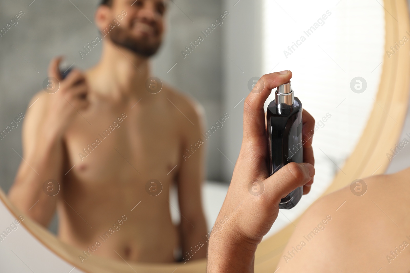 Photo of Man spraying luxury perfume near mirror indoors, closeup