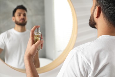 Photo of Man spraying luxury perfume near mirror indoors, closeup