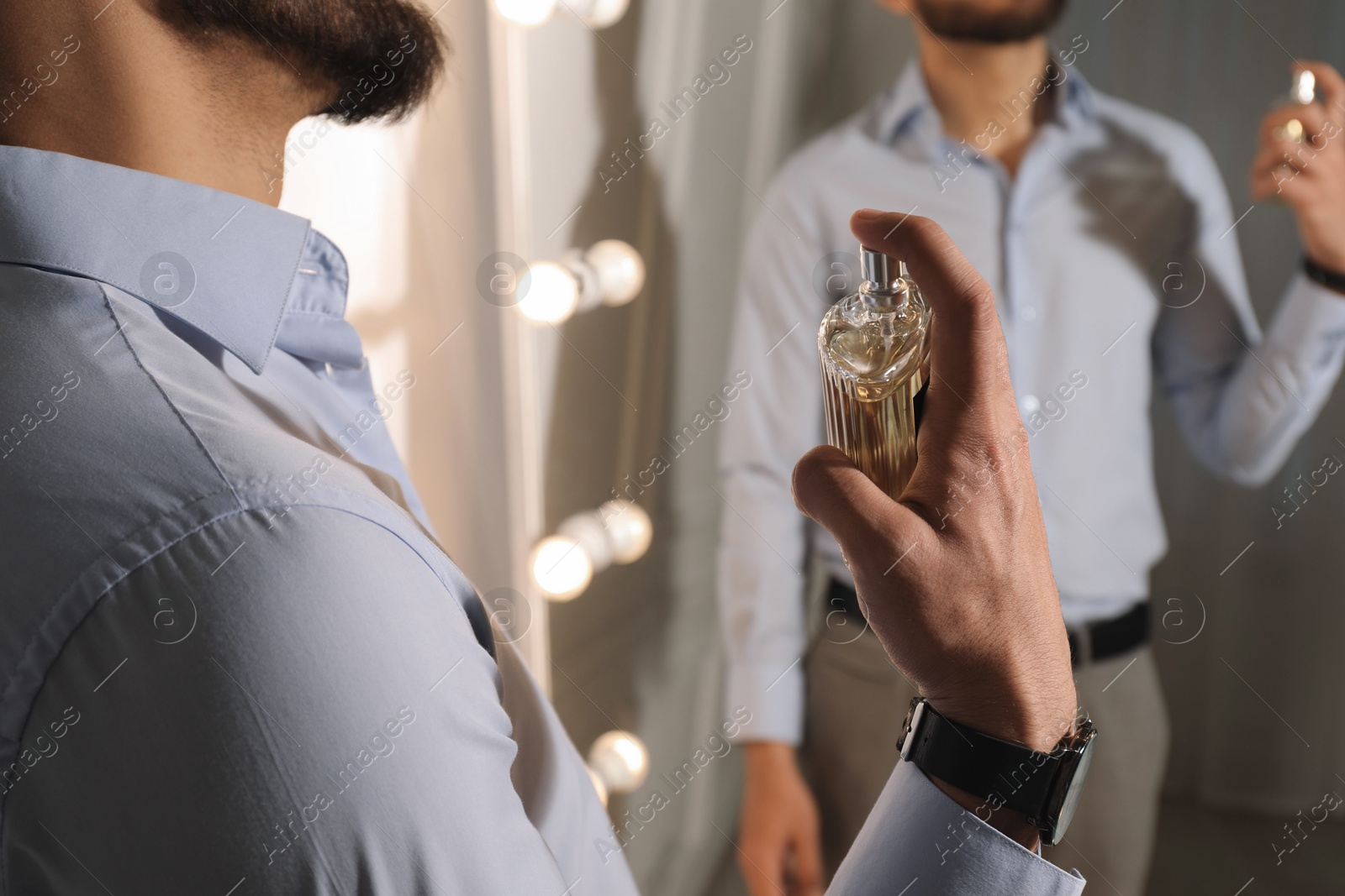 Photo of Man spraying luxury perfume near mirror indoors, closeup