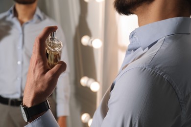 Man spraying luxury perfume near mirror indoors, closeup