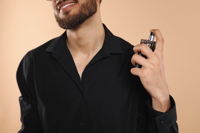 Man spraying luxury perfume on beige background, closeup