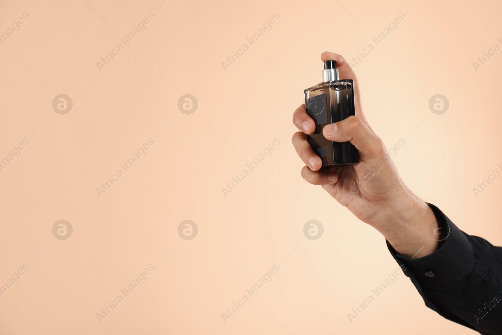 Photo of Man spraying luxury perfume on beige background, closeup. Space for text