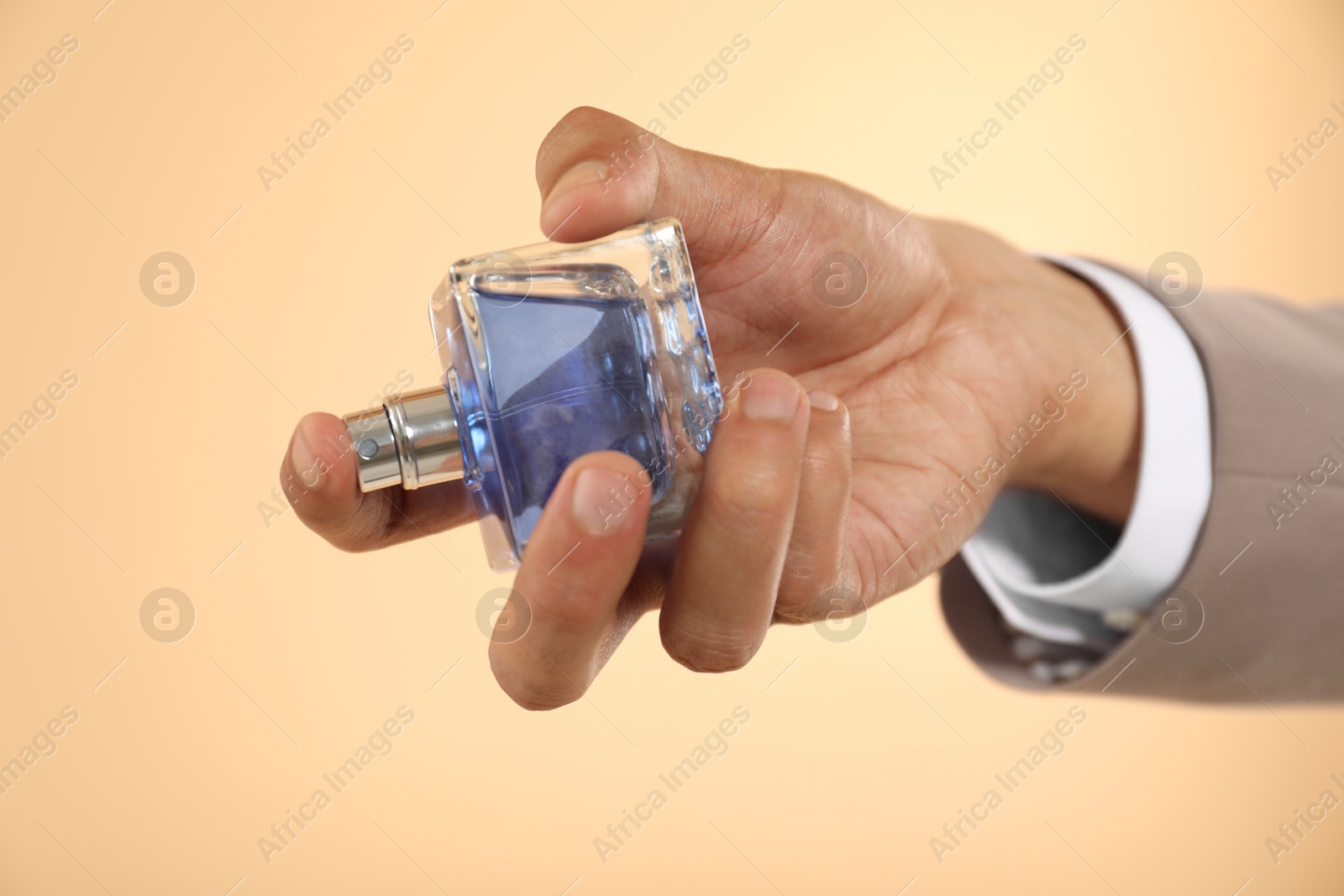 Photo of Man spraying luxury perfume on beige background, closeup