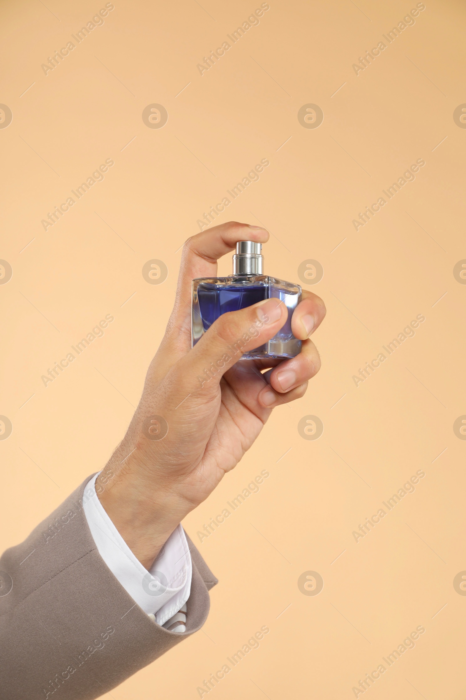Photo of Man spraying luxury perfume on beige background, closeup