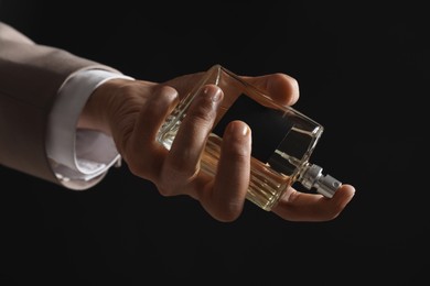 Photo of Man spraying luxury perfume on dark background, closeup