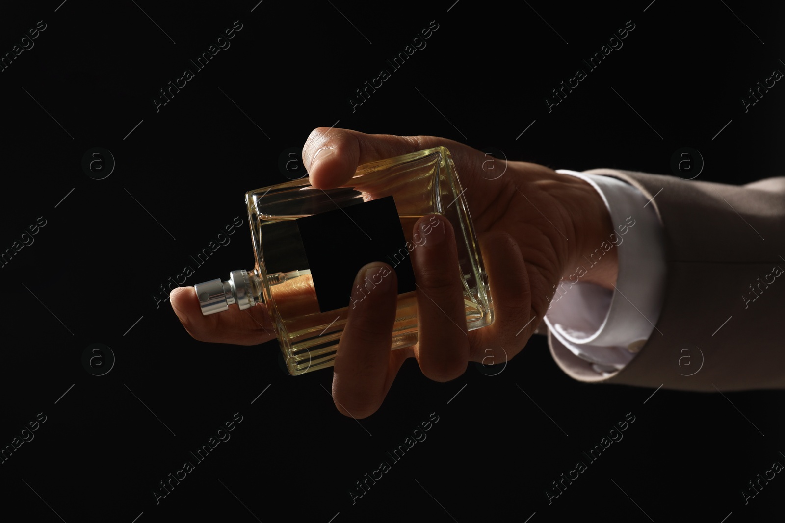 Photo of Man spraying luxury perfume on dark background, closeup