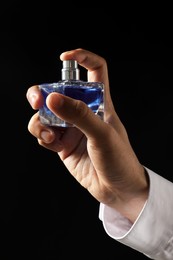 Photo of Man spraying luxury perfume on dark background, closeup