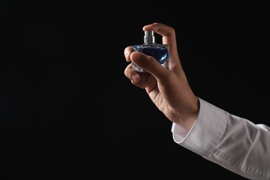 Photo of Man spraying luxury perfume on dark background, closeup. Space for text