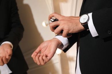 Photo of Man spraying luxury perfume near mirror indoors, closeup