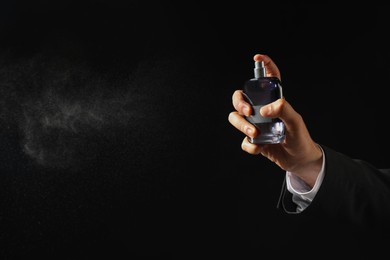 Photo of Man spraying luxury perfume on dark background, closeup. Space for text