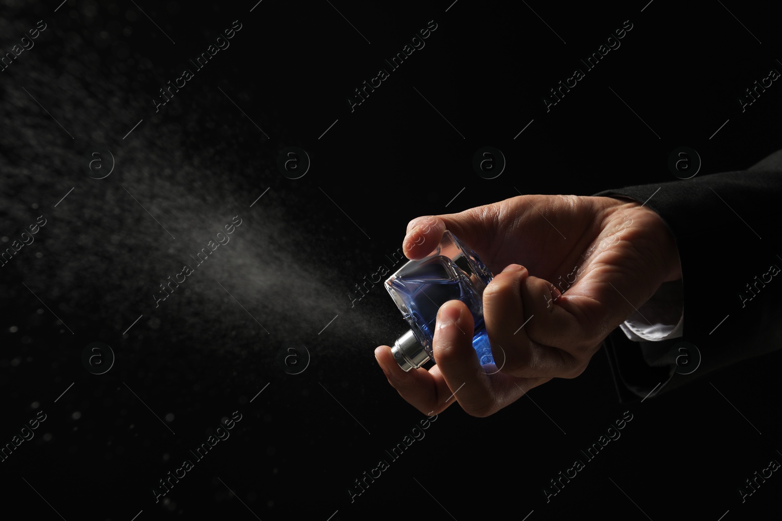 Photo of Man spraying luxury perfume on dark background, closeup. Space for text